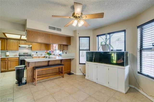 kitchen with kitchen peninsula, ceiling fan, stainless steel range oven, a breakfast bar area, and light tile patterned flooring