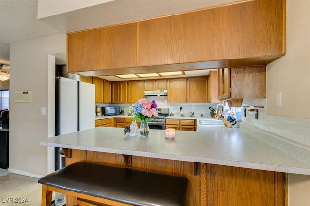 kitchen with stainless steel range, sink, white refrigerator, kitchen peninsula, and a kitchen bar