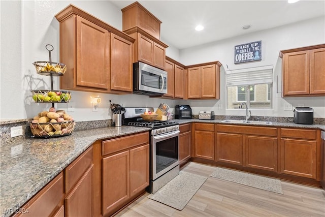 kitchen featuring appliances with stainless steel finishes, dark stone counters, brown cabinets, and a sink