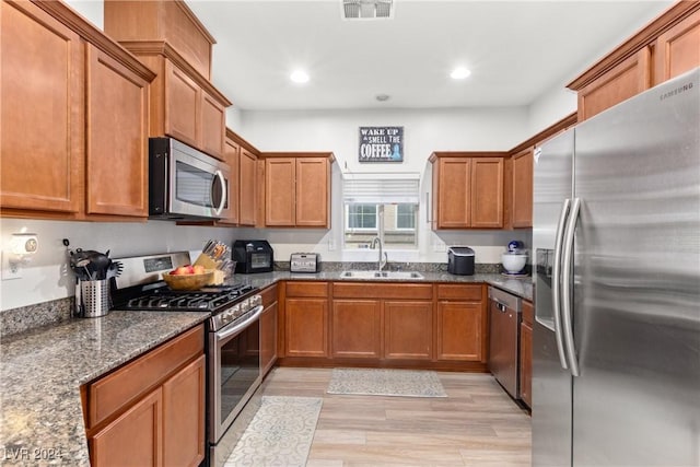 kitchen with visible vents, brown cabinetry, dark stone countertops, stainless steel appliances, and a sink