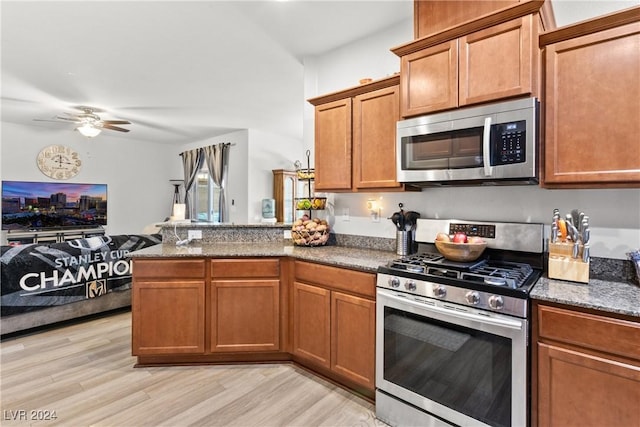 kitchen featuring dark stone counters, appliances with stainless steel finishes, open floor plan, a peninsula, and light wood-style floors