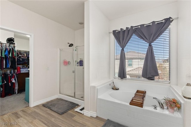 bathroom featuring a stall shower, a spacious closet, a bath, and wood finished floors