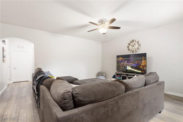 living room with light wood-style floors, ceiling fan, visible vents, and arched walkways