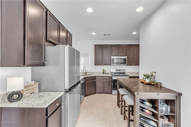 kitchen featuring sink, light tile patterned floors, dark brown cabinets, and appliances with stainless steel finishes