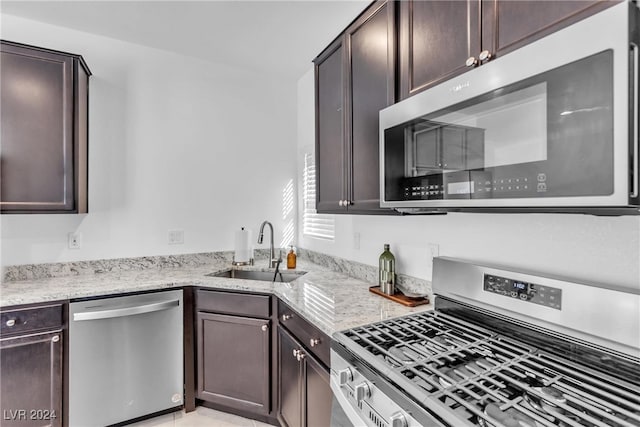 kitchen featuring light stone countertops, appliances with stainless steel finishes, dark brown cabinetry, and sink