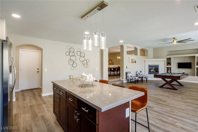 kitchen with ceiling fan, stainless steel fridge, light hardwood / wood-style floors, a kitchen bar, and a kitchen island