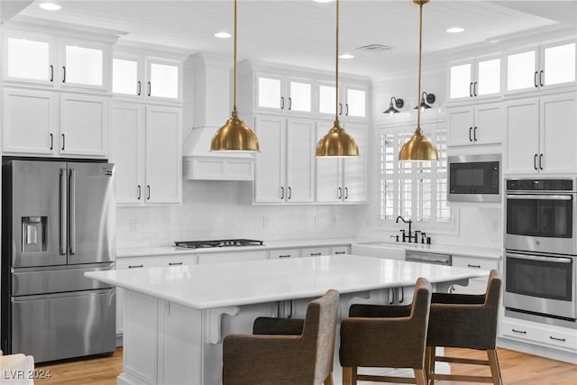 kitchen featuring white cabinetry, a center island, stainless steel appliances, light hardwood / wood-style floors, and a kitchen bar