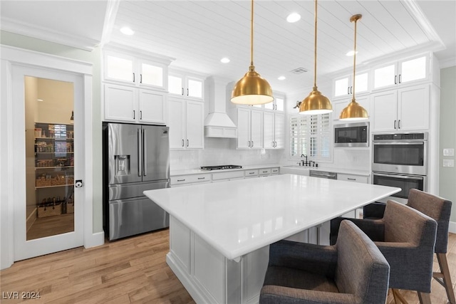 kitchen with custom exhaust hood, stainless steel appliances, decorative light fixtures, a center island, and light hardwood / wood-style floors