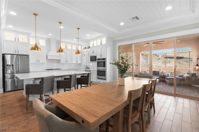 dining area featuring ceiling fan, sink, crown molding, a tray ceiling, and light wood-type flooring