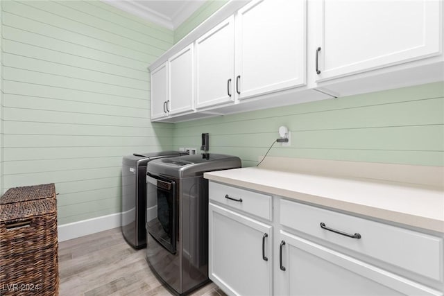 clothes washing area with wood walls, cabinets, light hardwood / wood-style flooring, washing machine and dryer, and ornamental molding