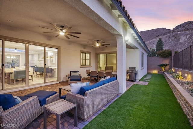 patio terrace at dusk with outdoor lounge area, ceiling fan, a grill, and a yard