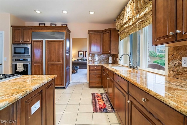 kitchen featuring sink, light tile patterned floors, built in appliances, light stone counters, and tasteful backsplash