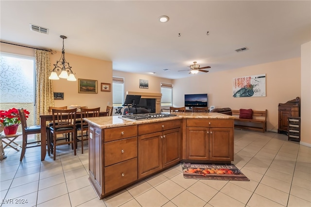 kitchen with light stone counters, decorative light fixtures, stainless steel gas cooktop, and light tile patterned floors