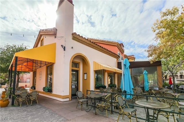 rear view of property with stucco siding, a patio, outdoor dining space, and a tile roof