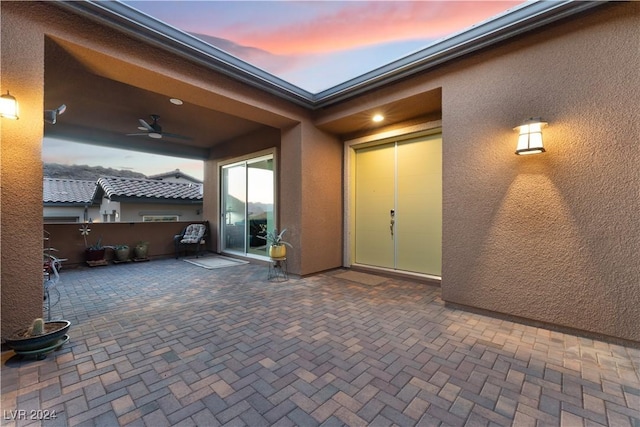 patio terrace at dusk featuring an attached garage and a ceiling fan