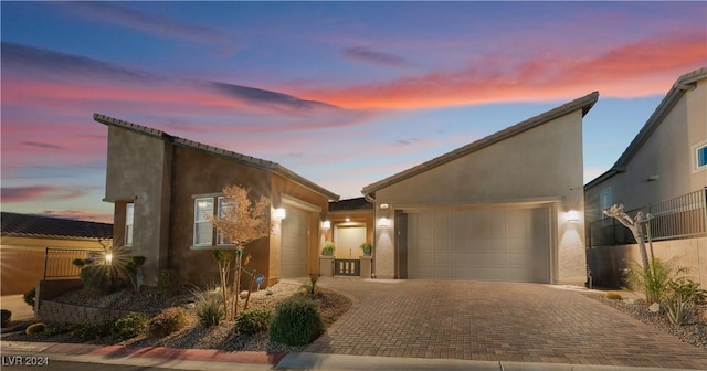 mid-century inspired home featuring stucco siding, decorative driveway, a garage, and fence