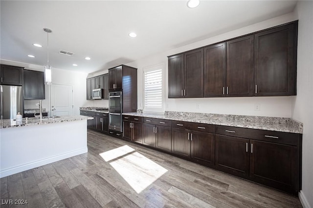 kitchen featuring appliances with stainless steel finishes, light stone counters, dark brown cabinetry, light hardwood / wood-style floors, and hanging light fixtures