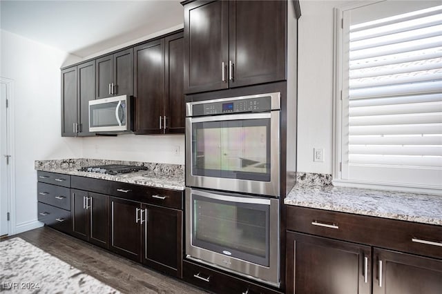 kitchen with dark brown cabinets, light stone countertops, stainless steel appliances, and dark wood-type flooring