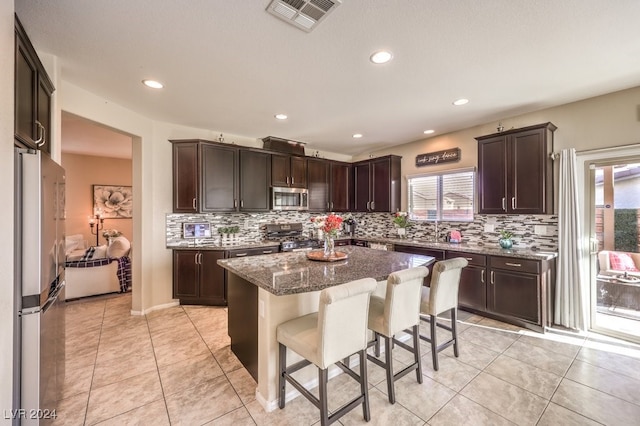 kitchen with a breakfast bar, a center island, backsplash, dark stone countertops, and stainless steel appliances