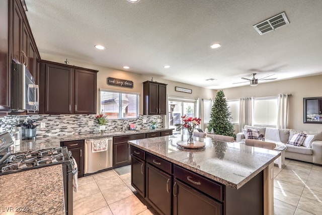 kitchen with dark brown cabinets, stainless steel appliances, ceiling fan, sink, and a center island