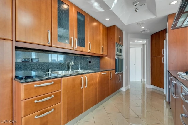 kitchen featuring tasteful backsplash, stainless steel appliances, sink, light tile patterned floors, and dark stone countertops