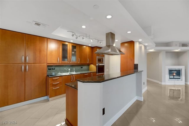 kitchen featuring decorative backsplash, appliances with stainless steel finishes, dark stone counters, island range hood, and sink