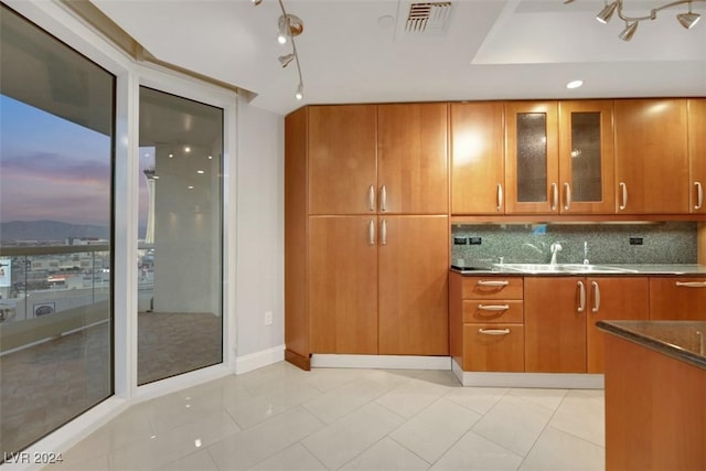 kitchen with sink, rail lighting, dark stone countertops, decorative backsplash, and light tile patterned flooring