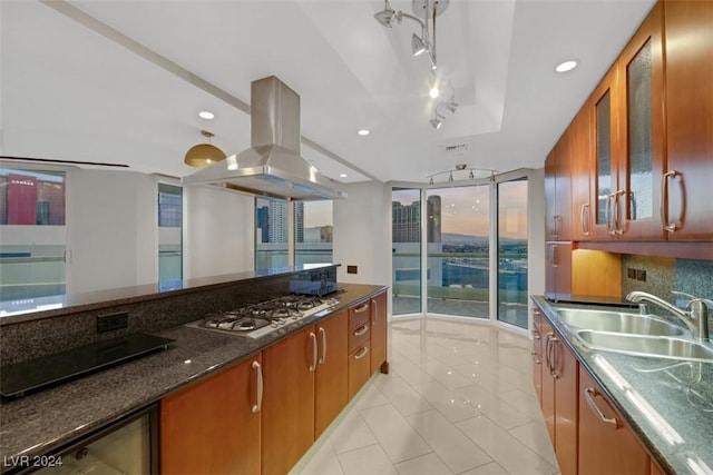 kitchen featuring backsplash, dark stone counters, island range hood, sink, and stainless steel gas stovetop