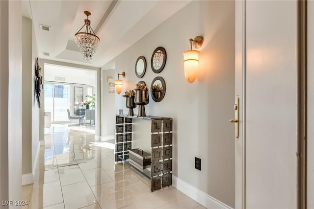 hall featuring a notable chandelier, a raised ceiling, visible vents, and baseboards