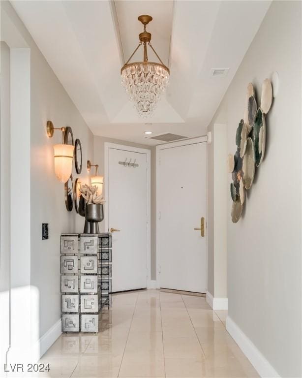 hall featuring light tile patterned floors, visible vents, baseboards, and a chandelier