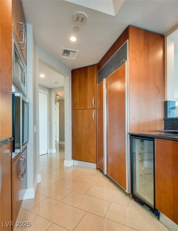 hallway with beverage cooler, light tile patterned floors, visible vents, and baseboards