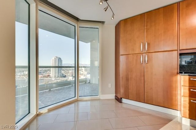 doorway with light tile patterned floors, baseboards, floor to ceiling windows, a view of city, and rail lighting