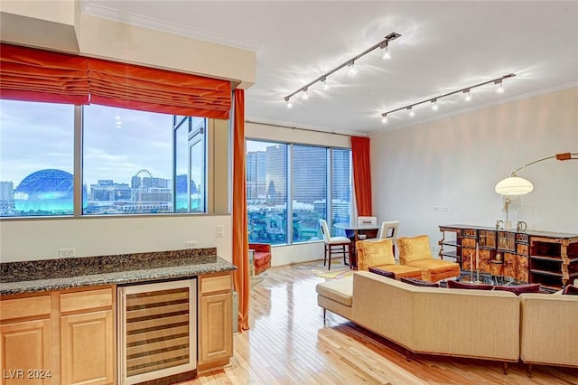 living room featuring rail lighting, beverage cooler, crown molding, light hardwood / wood-style floors, and indoor bar