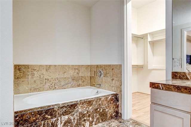 bathroom with vanity, wood-type flooring, and a relaxing tiled tub