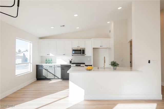 kitchen with stainless steel appliances, tasteful backsplash, light hardwood / wood-style floors, lofted ceiling, and white cabinets