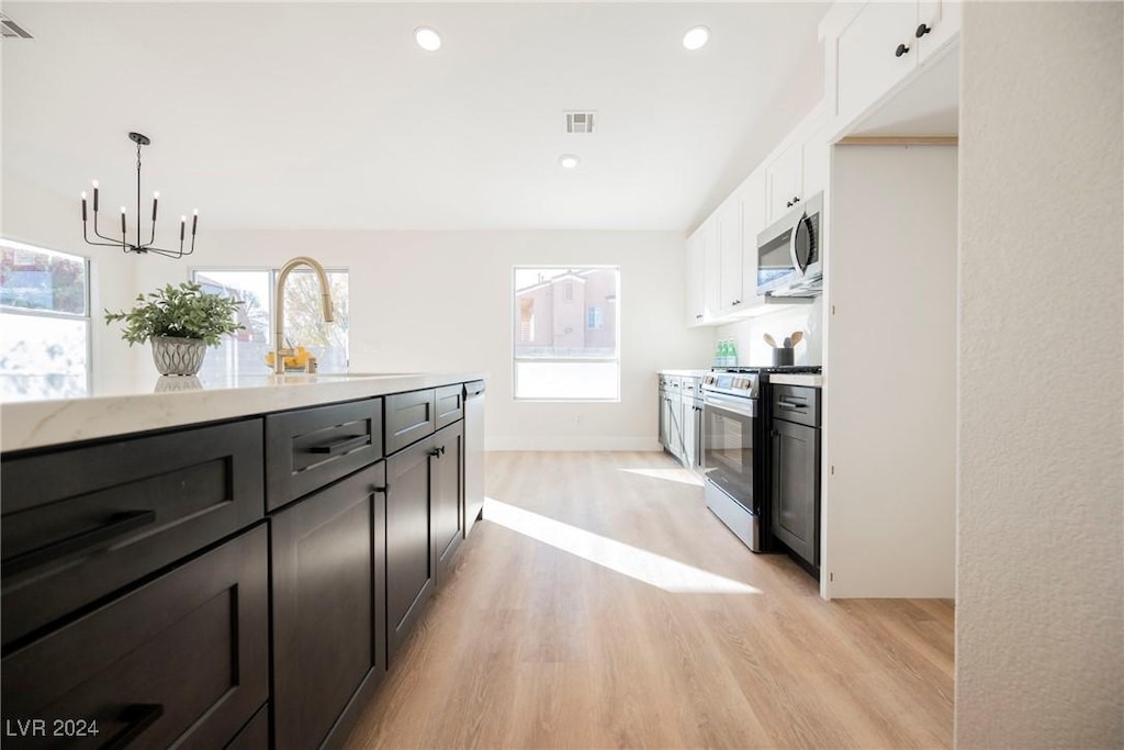 kitchen featuring white cabinets, appliances with stainless steel finishes, light hardwood / wood-style floors, and pendant lighting