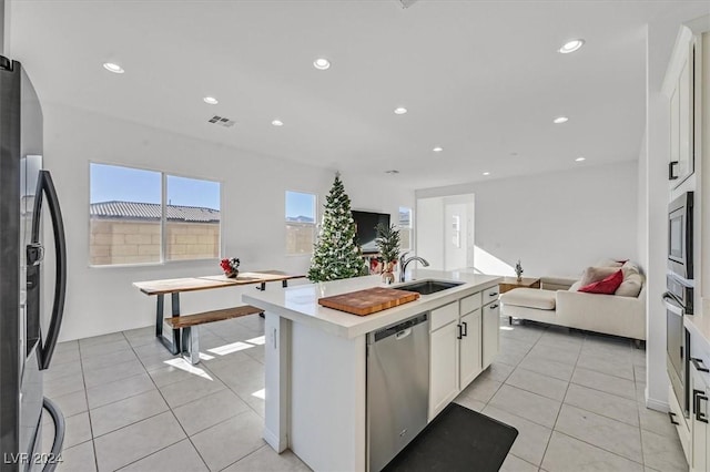 kitchen with stainless steel appliances, sink, light tile patterned floors, a center island with sink, and white cabinets