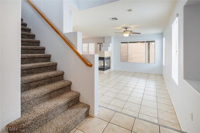 stairs featuring a tile fireplace, tile patterned floors, and ceiling fan