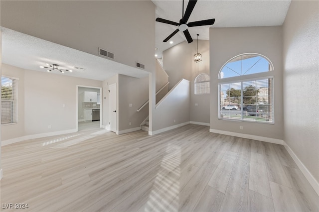 unfurnished living room with ceiling fan, light hardwood / wood-style flooring, high vaulted ceiling, and a textured ceiling