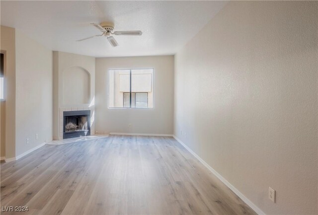 unfurnished living room with a tile fireplace, light wood-type flooring, and ceiling fan