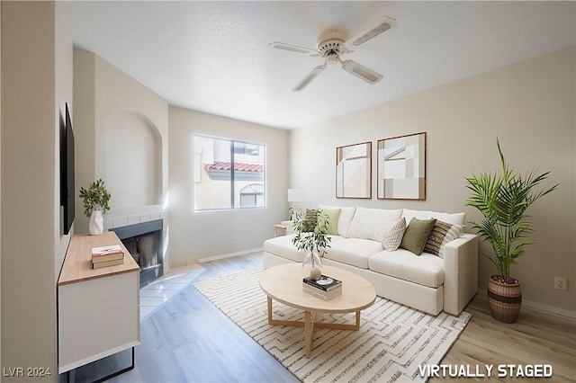 living area featuring light wood-type flooring, baseboards, a ceiling fan, and a tiled fireplace