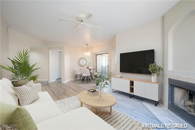 living room featuring light wood-type flooring, a ceiling fan, and a tile fireplace