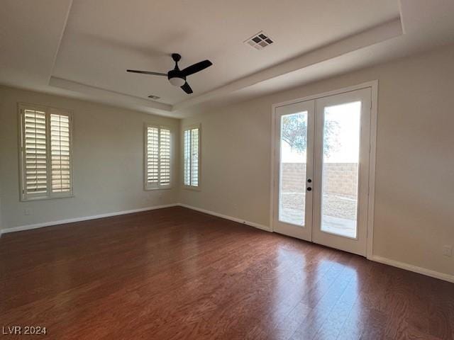 empty room featuring ceiling fan, a healthy amount of sunlight, a raised ceiling, and french doors