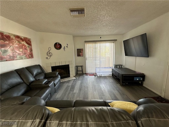 living room featuring a tile fireplace, dark wood-type flooring, and a textured ceiling