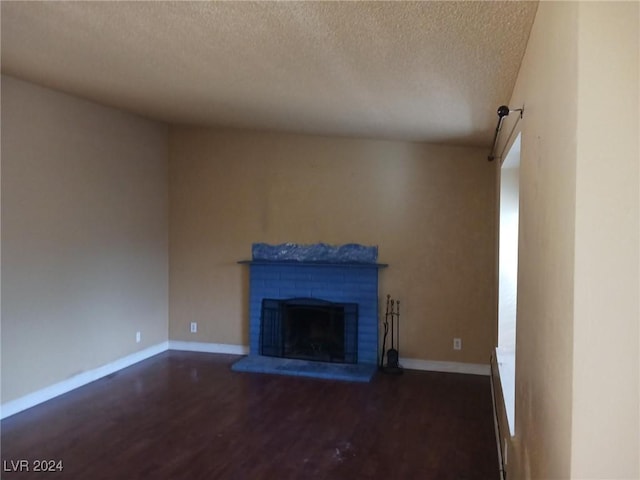 unfurnished living room featuring dark hardwood / wood-style floors, a textured ceiling, and a brick fireplace