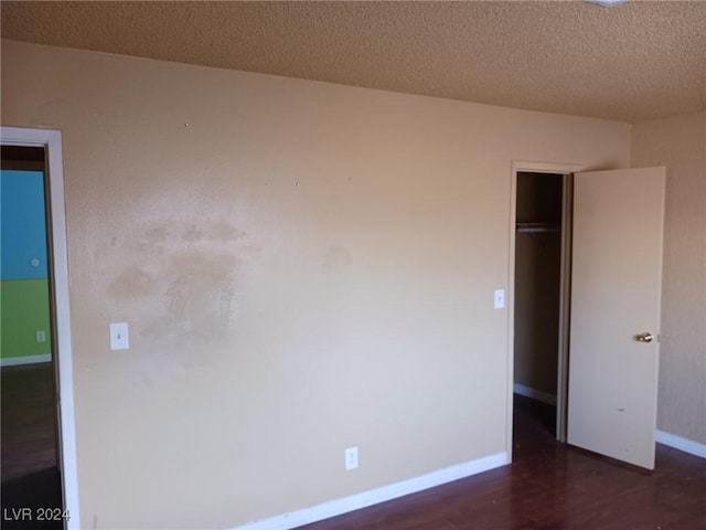 unfurnished bedroom featuring a textured ceiling, dark hardwood / wood-style flooring, and a closet