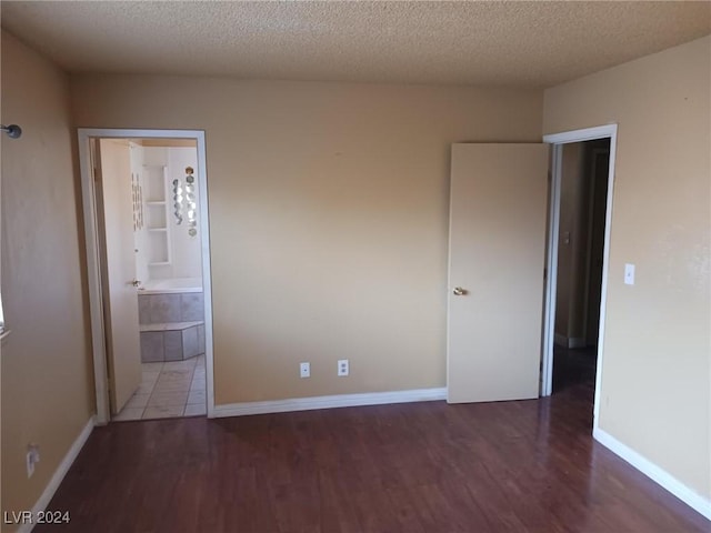 unfurnished bedroom featuring ensuite bath, dark wood-type flooring, and a textured ceiling