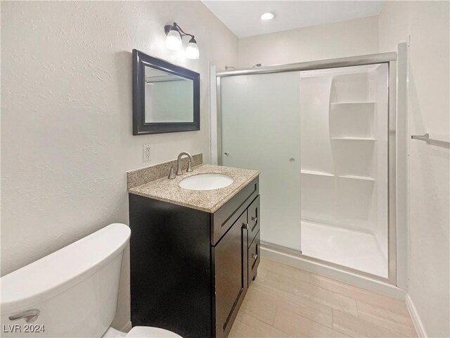 bathroom with wood-type flooring, vanity, toilet, and a shower with door