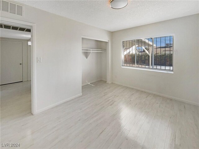 unfurnished bedroom with a closet, a textured ceiling, and light hardwood / wood-style flooring