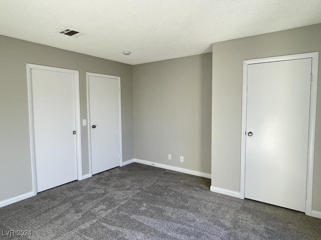 unfurnished bedroom with a textured ceiling and dark colored carpet